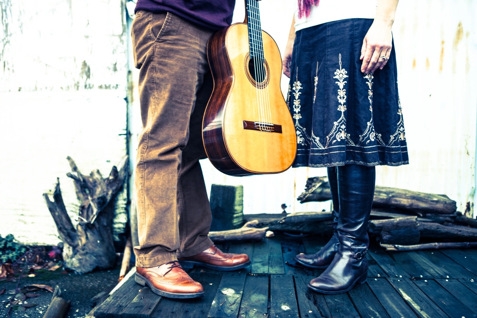 Chérie L. Hughes and Roberto Limón shown from the waist down, his classical guitar between them, on a weathered wooden deck